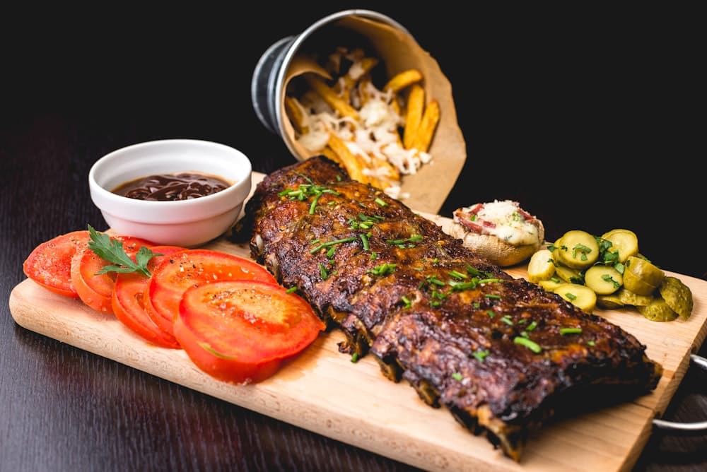 Carne de cerdo lacada brillante sobre tabla, con tomates y pepinillo al lado
