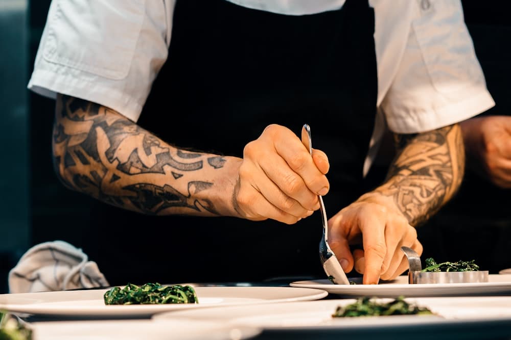 Manos del cocinero emplatando con cuidado sobre plato blanco